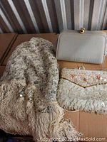 Shawl with lace, sequins, and fringe next to two purses: one white textured clasp purse and one embroidered fabric clutch purse with sequins.