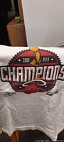 Close-up photo of the white 2006 NBA Champions Miami Heat T-shirt showing design details including the NBA trophy and team logo.