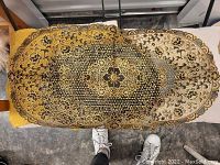 Photo of an oval gold table center mat with intricate floral and lace-inspired embroidery patterns.