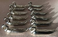 Twelve silver plated swan-shaped utensil rests arranged in rows on a countertop, showing the shape and size of each rest.
