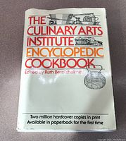 Front cover of the cookbook showing title and editor's name with white background and illustrative cooking tools.