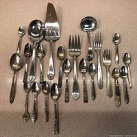 Top view of all 22 cutlery pieces arranged on a surface, showing spoons, forks, ladle, cake server, and knife.