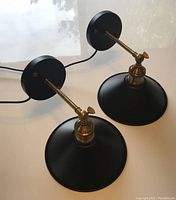 Pair of black shade wall sconces with brass arms and back plates shown from the top and side, displaying overall design and wiring.