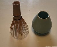 Green glazed ceramic stand and bamboo tea whisk side by side on a flat surface.
