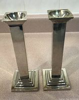 Pair of tall silver plated candlesticks standing upright showing full height and rectangular column design with stepped square base and square top.