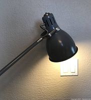 Close-up of the lamp head showing the metal conical shade with ventilation slots, painted grey.