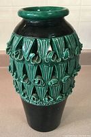 Front view of tall ceramic vase with green raised leaf and scroll decoration on black glazed background.