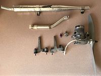 Full view of OS RX140 engine with mounts, manifold, exhaust pipes, and wooden propeller laid out on surface.