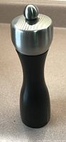 Side view of the Peugeot pepper grinder showing black lacquered base and stainless steel top with knob.