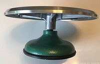 Side view of the revolving cake decorating stand showing the green base with rubber suction cup and polished aluminum top edge.