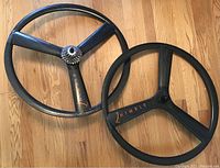 Two carbon fibre Nimble three-spoke bicycle rims laid on wooden floor, with SRAM cassette on one rim.