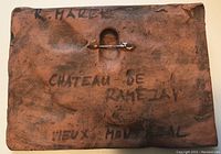 Back view showing stamped and hand-written markings including artist's signature and location references, with attached safety pin for hanging.