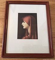 Full view of the framed print showing the portrait of a woman in a red hood, with wooden frame and textured mat.