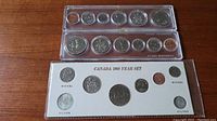 Three coin sets displayed on wooden surface; top and middle sets in transparent plastic holders, bottom set in white cardboard holder labeled 'CANADA 1968 YEAR SET'.