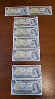 Eight 1973 Bank of Canada one dollar bills laid out on a wooden surface, showing front side with Queen Elizabeth II portrait and details.