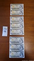 Eight 1973 Bank of Canada one dollar bills laid out on a wooden surface, showing the front side with the image of Queen Elizabeth II and bilingual text.