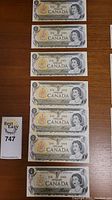 Seven Canadian one dollar bills from 1973 displayed face up, showing Queen Elizabeth II portrait and bilingual text.