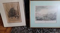 Two framed English art prints, one of a building under construction and one of a coastal harbor scene