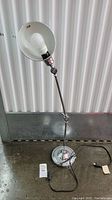 Chrome adjustable desk lamp with bulb exposed, articulating arm and round base, sitting on concrete floor against a corrugated metal wall.