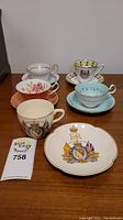 Overview of 5 teacups arranged with saucers, showing a mix of floral and commemorative designs including England flag and coronation imagery.