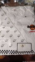New white chefs coat in original bag with black and white checkered trim and small chef hat print on packaging.