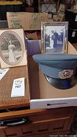 Overall lot with two framed photos and green military peaked cap on a table showing labels and surrounding items