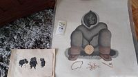 Two prints side by side: large print of hooded figure at right and smaller three-figure print at left