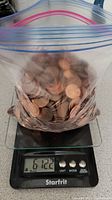 Ziploc bag with copper-colored pennies on a digital scale showing weight 612.2 grams.