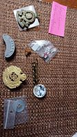 Overview of seven assorted pins, including a large gold-tone military crest, a curved silver-tone pin, and a pack with small pins.