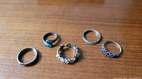 Five sterling silver rings arranged on wooden surface showing overall designs and color details of stones.
