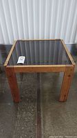 Front view of square teak side table with black glass top