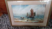 Framed watercolor artwork showing several sailboats with tall sails on the sea, placed on a carpeted floor.