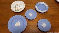 Lot of five Wedgwood miniature plates including four blue Jasperware with white relief motifs and one floral design plate with gold rim.