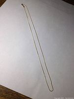 Full length view of delicate 14K gold chain necklace laid flat on white background.