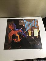 Front side of the vinyl album cover featuring David Bowie with boxing gloves and stylized title.