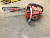 Red Homelite XL 2 gas chainsaw with newer bar and chain, visible wear on protective metal handle guard and body surface.