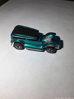 Side front angle showing metallic teal blue Die cast Hot Wheels car with chrome engine and exhaust, redline wheels.