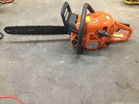 Full side view of chainsaw on concrete floor showing bar, chain, housing and front handle
