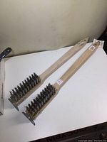 Pair of two large Felton BBQ brushes with long wooden handles laid flat showing full length