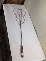 Full length view of antique metal rug beater with wood handle, showing overall structure and wear.