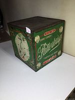 Front and side view of green square metal candy tin with Patterkrisp branding and a child’s face graphic.