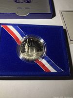 Top-down photo of 1986 Liberty Half Dollar proof coin in clear round capsule on blue velvet with patriotic ribbon.