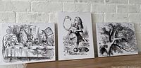 Set of three Alice in Wonderland themed black and white canvas art prints against white brick wall