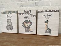 Three animal canvas wall arts on a brick background showing hippo, lion, and giraffe with banners and motivational texts