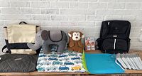 Overview of entire lot showing backpacks, plush toys, duvet set, placemats, baby hangers, and safety system