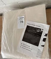 Photo of the folded beige replacement canopy cover in clear packaging with instruction sheet visible.