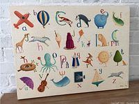 Front view of the Oopsy Daisy Crackle Alphabet canvas showing colorful illustrated alphabet with various associated objects on a cream background