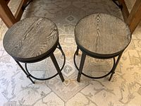 Pair of stools showing the wood grain round seats and black metal legs with foot rests.