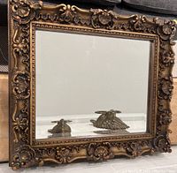 Front view of the rectangular mirror showing detailed ornate gold carved wooden frame and beveled glass reflecting objects.