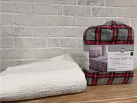 Twin size Huntington Home flannel sheet set in original packaging with a red, gray, and black plaid pattern, photographed next to a folded white quilted throw.